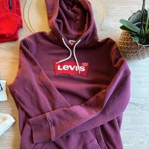 Vinröd hoodie från Levi's - Säljer en vinröd hoodie från Levi's med klassisk logga framtill. Tröjan har huva med snörning och en stor magficka. Perfekt för dig som gillar en avslappnad och cool stil.