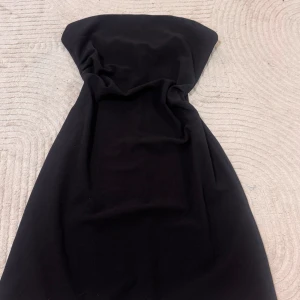 Svart axelbandslös klänning Koton - Svart axelbandslös klänning från Koton i stilren design. Klänningen är figurnära och har dragkedja bak för enkel påklädning. Perfekt för dig som gillar minimalistisk och elegant stil. Materialet känns mjukt och följsamt mot kroppen.