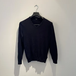 Mörkblå v-ringad tröja Massimo Dutti - Mörkblå v-ringad tröja från Massimo Dutti i bomull och silke. Långa ärmar med bruna mockadetaljer på armbågarna ger en snygg touch. Perfekt för dig som gillar klassisk stil med en twist. Inga defekter hör av er vid frågor