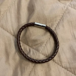 Brunt flätat armband  - Snyggt armband i mörkbrunt flätat material. Perfekt accessoar för en enkel men cool look.  Ej äkta läder gjort av plast 