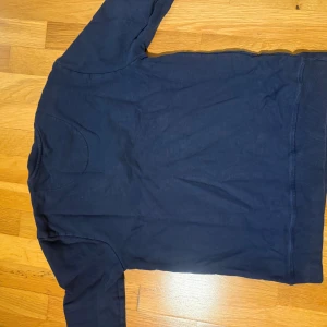 Mörkblå långärmad tröja  - Snygg mörkblå långärmad tröja med diskret mönster och rund hals. Tröjan har en mjuk bomullskänsla och subtilt broderad logga framtill. Perfekt för dig som gillar stilrena och klassiska plagg.