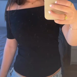 Svart offshoulder topp - Snygg svart offshoulder topp med korta ärmar och tight passform. Perfekt att styla med jeans eller kjol för en trendig look. Enkel och stilren design som framhäver axlarna.