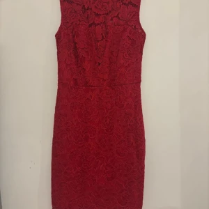 Röd spetsklänning med blommönster - Säljer en röd kortklänning i spets med blommigt mönster. Klänningen är ärmlös och har en figurnära passform. Perfekt för dig som vill sticka ut med en elegant och feminin look. Dragkedja baktill för enkel påklädning.