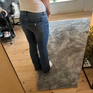 Blåa bootcut lowwaist jeans  - Säljer ett par klassiska blå jeans med bootcut passform och låg midja. Jeansen har snygga fickor med lock och knapp bak (endast använda 2 gånger)