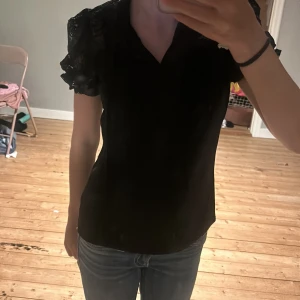 Svart blus med spetsärmar från Boohoo - Säljer en svart blus från Boohoo med puffiga spetsärmar och spetsdetaljer. Blusen har en liten krage och knytband framtill. Inte andvänd jättemycket så ganska bra skick 