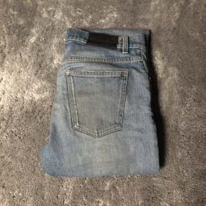 Ljusblå jeans från J.Lindeberg 30/32 - Snygga ljusblå jeans från J.Lindeberg i klassisk femficksmodell. Jeansen har raka ben och normal passform, tillverkade i mjukt denimtyg med  slitningar i designen för en avslappnad look. Perfekta för dig som gillar stilrena och tidlösa jeans.