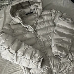 Ljusgrå pufferjacka från Zara - Säljer en ljusgrå pufferjacka från Zara i storlek M men den passar som S. Jackan har huva, dragkedja framtill och elastiska muddar vid ärmslut och nederkant. Perfekt för kyliga dagar och riktigt skön att bära. Stilren och enkel design som passar till det mesta.