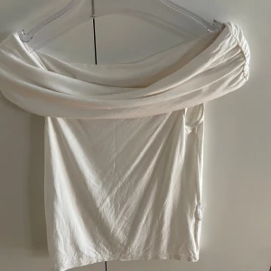 Vit offshoulder topp från Amisu - Säljer en vit offshoulder topp från Amisu i storlek S. Toppen har en bred, draperad krage som vilar snyggt över axlarna och ger en cool, trendig look. Materialet är mjukt och stretchigt, perfekt för att skapa en stilren outfit.