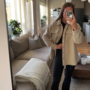 Beige overshirt från & Other Stories - Overshirt i beige från & Other Stories med klassisk krage, två stora bröstfickor och silvriga knappar framtill. Jackan är i ullmix och har en loose passform med långa ärmar. Storlek 36