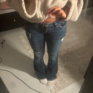 Blå bootcut jeans med slitningar - Snygga blå jeans med bootcut-modell och slitna detaljer på knäna och låren. Jeansen har klassisk femficksdesign, kontrastsömmar och är tillverkade i ett stretchigt denimtyg som sitter skönt. 