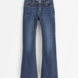 Mörk Blå bootcut jeans med låg midja - Snygga blå jeans med bootcut passform och låg midja. Jeansen har klassiska fem fickor, kontrastsömmar och är tillverkade i mjukt denimtyg. Perfekta för dig som gillar en retroinspirerad look med utsvängda ben.