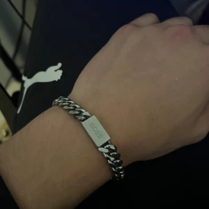 Silverfärgat armband från BOSS - Stilrent armband från BOSS i silverfärgad metall med kraftig kedja och rektangulär platta där BOSS-loggan är ingraverad. Perfekt accessoar för dig som gillar en clean och modern look.