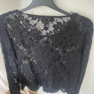 Svart spetsblus med blommönster - Snygg svart blus i spets med blommigt mönster och långärmad design. Blusen har rund halsringning och är genombruten med fina detaljer i spetsen. Perfekt för dig som gillar en elegant och trendig look.