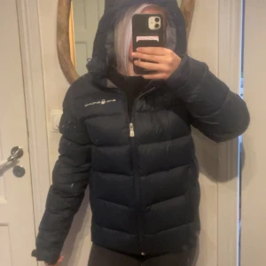 Mörkblå dunjacka från Sail Racing storlek S - Säljer en mörkblå dunjacka från sail racing. I bra skick och inte mycket använd då den inte längre är min stil. Det är ett litet hål i bak på ryggen som är lagat, och syns bara lite i vissa ljus men inte alls märkvärdigt, luvan täcker inprincip hela lagningen. 