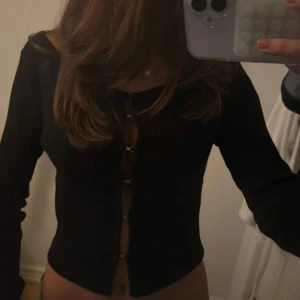 Svart långärmad topp med spännen  - Säljer en svart långärmad topp med öppen front med spännen.