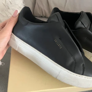 Axel Arigato dam skor - Stilrena svarta sneakers från Axel Arigato i skinn med vit platt sula. Använd fåtal gånger. Inga tecken på användning. Storlek 37 men passar mig som har 38 vanligtvis. Originalbox och påse medföljer. Kvitto finns. Pris går att diskutera vid snabbaffär.