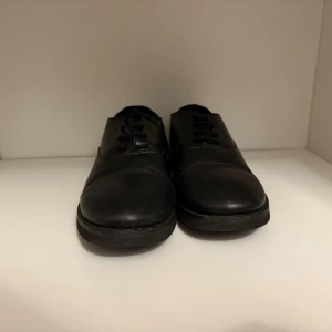 Svarta klassiska skinnskor med snörning - Snygga svarta skinnskor med låg klack och rund tå. Skorna har klassisk design med snörning framtill och en stilren look som passar till många outfits. Tillverkade i slätt skinn och har en platt sula för bekväm känsla hela dagen.