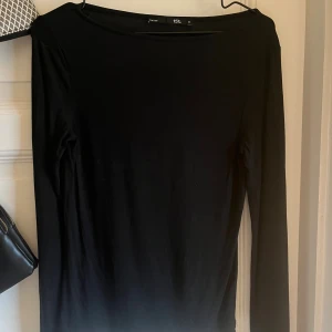 Svart långärmad tröja 157 - En stilren svart långärmad tröja från 157 med enkel och rak passform. Klänningen har rund halsringning och är tillverkad i ett mjukt material som känns skönt mot huden. Perfekt för dig som gillar minimalistisk och clean stil.