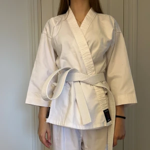 Vit karate-gi från Budo-Nord Empi - Säljer TVÅ likadana karatedräckter. Båda för 500. Karatedräkt från Budo-Nord Empi i helvitt, tillverkad i kraftig bomull. Klassisk omlottkavaj med vit bälte och raka byxor. Perfekt för träning inom kampsport. Snygg och stilren design med broderad etikett på jackan och bältet. 