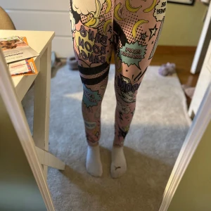 Stronger leggings med pop art-mönster - Leggings från Stronger i storlek small med färgglatt pop art-inspirerat mönster i rosa, svart, gult och blått. Tajt passform och hög midja, tillverkade i polyester och elastan. Perfekta för dig som vill sticka ut på gymmet eller i vardagen.