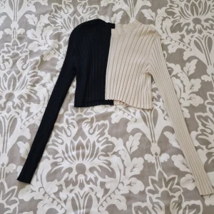 Tvåfärgad ribbad crop-top från Monki - Säljer en ribbstickad långärmad tröja från Monki i storlek L. Tröjan är croppad och har en cool tvåfärgad design med ena halvan svart och andra halvan beige. Oanvänd och tvättad 1 gång.