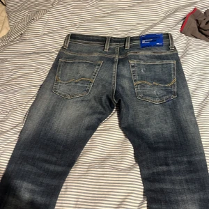 Blå jeans Lucky Brand med slitningar stl 29/30 - Säljer ett par blå jeans från Lucky Brand med snygga slitningar och rivna detaljer framtill. Jeansen har klassiska bakfickor med gul söm och normal passform. Perfekta för dig som gillar en avslappnad och trendig look.