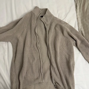 Beige stickad kofta med dragkedja - Säljer en beige stickad kofta från Lager 156 med dragkedja framtill och hög krage. 