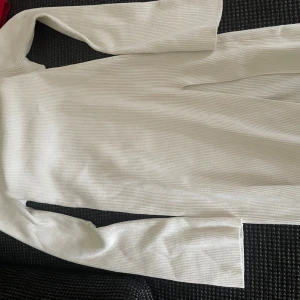 Vit ribbad långärmad klänning H&M - Långärmad vit ribbad klänning från H&M  i storlek S. den är en midklänning så slutar vid vaderna. Har en slits vid lårna. Aldrig använd