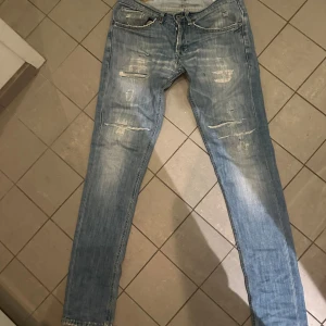 Dondup storlek 29 - Säljer ett par ljusblå jeans med slitningar och distressed detaljer på både fram- och baksida. Jeansen har klassisk femficksdesign, normal passform och raka ben. Materialet är mjukt denim som ger en avslappnad vibe. 