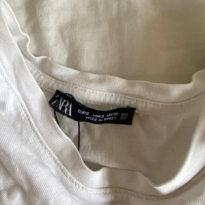 Vit blus med spetsärmar från Zara - Supersöt vit blus från Zara med broderade spetsärmar som ger en romantisk vibe. Blusen har rund halsringning och är tillverkad i mjuk bomull. Perfekt för dig som gillar feminina detaljer och vill ha något extra till din outfit.