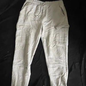 Grå cargobyxor från Primark Care XL - Grå cargobyxor från Primark Care i storlek XL. Byxorna har elastisk midja med snörning, stora sidofickor med lock och resår vid bensluten. Tillverkade i mjukt bomullsmaterial för en chill och bekväm stil.