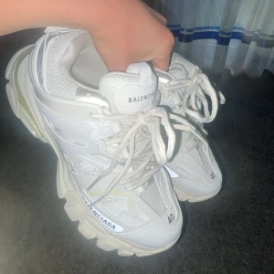 Balenciaga vita chunky sneakers - Säljer ett par vita chunky sneakers från Balenciaga med coola detaljer och grov sula. Skorna har snörning, meshpaneler och Balenciaga-logga på sidan och plösen. Perfekta för dig som gillar statement-skor och streetstyle.