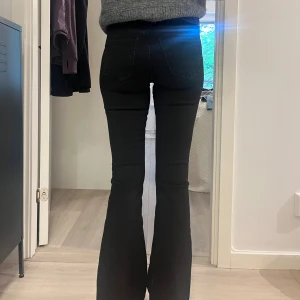 Svarta bootcut jeans med låg midja - Säljer ett par svarta jeans med bootcut-modell och låg midja. Jeansen har klassiska bakfickor och sitter tight över låren innan de släpper ut vid vaden. Perfekta för dig som gillar en stilren och tidlös look.