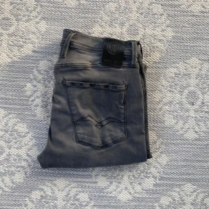 Replay Anbass Hyperflex grå jeans - Säljer ett par grå Replay Anbass Hyperflex jeans i storlek 32/36. De har klassisk femficksdesign, raka ben och snygga detaljer på bakfickan. Jeansen är tillverkade i stretchigt material för extra komfort och har en modern, smal passform. Passar mig och jag är 188cm/80kg