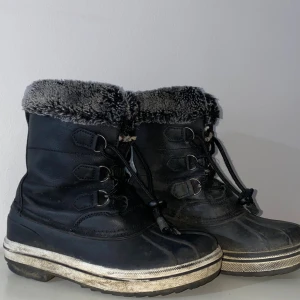 Svarta vinterboots från McKinley - Svarta vinterboots från McKinley med grått foder i pälsimitation och snörning framtill. Skorna har en robust platt sula och är perfekta för kalla dagar. Materialet är en mix av syntet och textil, med extra värmande insida. En svart vinterskor för barn med storlek 33/34. Som ni ser i bilden så är det ganska bra och håller fötterna varma. Annars meddela mig gärna för mer info! 