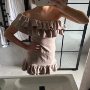 Beige offshoulder volangklänning - Supersöt beige kortklänning med offshoulder och dubbla volanger upptill samt volangkant nertill. Klänningen har en figurnära passform och är perfekt för dig som gillar en feminin och trendig stil. Materialet känns lätt och luftigt.