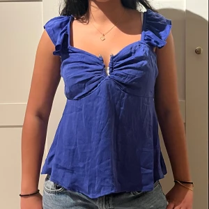 Helt nytt blå linnetopp med volangdetaljer med prislapp  - Snygg blå linnetopp med volangdetaljer på axelbanden och rynkad byst med dekorativa pärlor framtill. Toppen har en luftig passform och är perfekt för varma dagar. Styla med jeans eller kjol för en trendig look. Helt ny med prislappen kvar !!! Köpt från vero moda 