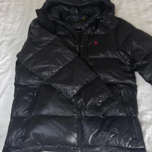 Polo Ralph Lauren Glossy Jacka Svart Medium - Svart Polo Ralph Lauren Glossy Jacka i storlek Medium.   Endast testad och icke använd, jackan är i nyskick och fri från defekter! Säljes då jag köpt ny jacka.  Finns att hämta i Jönköping och kan fraktas. Hör av dig vid frågor eller funderingar!