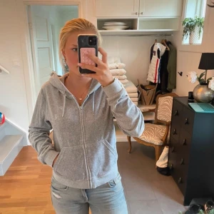 Grå hoodie från Juicy Couture - Säljer en grå hoodie från Juicy Couture med dragkedja och huva. Tröjan har långa ärmar, snörning i huvan och en snygg J-detalj på dragkedjan. Perfekt för chill dagar och enkel att matcha med jeans eller leggings.