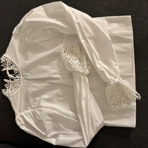 Vit spetsdetaljerad blus från H&M Divided - Superfin vit blus med långa ärmar från H&M Divided. Blusen har snygga spetsdetaljer vid halsringningen och ärmsluten samt knytning i ryggen.Tillverkad i bomull och perfekt för dig som gillar romantiska vibes.
