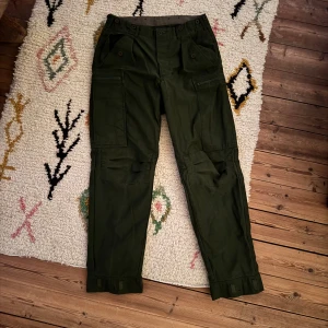 Gröna cargopants från Gulins Business - Äkta vintage-skatt! Svenska militära fältbyxor från 1989 av Design AB Gulins Business. Perfekta för dig som älskar äkta militaria, utility-mode eller bara vill ha ett par riktigt välgjorda, funktionella byxor med karaktär! Ursprung: Svenska försvaret, tillverkade 1989 	•	Tillverkare: Design AB Gulins Business 	•	Storlek: C50 (motsvarar ca midja 84-88 cm) 	•	Artikelnummer: MTR352045000-1 	•	Färg: Klassisk militär olivgrön 	•	Material: 50% bomull, 50% polyester