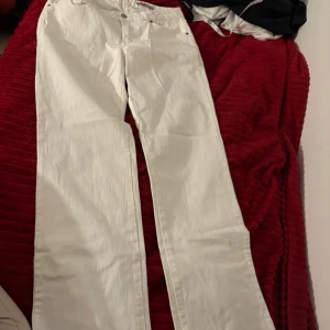 Vita raka jeans från Cue - Snygga vita jeans från Cue med klassisk femficksdesign och raka ben. Byxorna har diskreta sömmar på bakfickorna och silverfärgade nitar. Materialet är bomull med en lätt struktur som ger en cool känsla. Perfekta för dig som vill ha en clean och fräsch look.