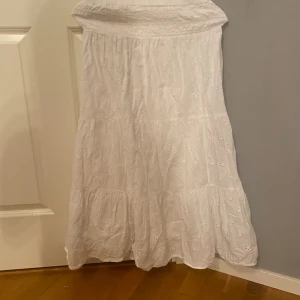 Vit långkjol med broderade detaljer Gina Tricot - Superfin vit långkjol från Gina Tricot med broderade blommor och smock i midjan. Kjolen har en luftig och flowy passform, perfekt för varma dagar. Tillverkad i bomull för en skön känsla och snygg look.