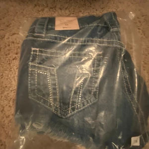 Blå jeansshorts med slitningar XS - Snygga blå jeansshorts i klassisk femficksmodell med slitna detaljer och fransad kant nedtill. Shortsen har låg midja, knapp och dragkedja framtill samt coola slitningar på framsidan för en avslappnad vibe. Perfekta för varma dagar och chill stil. Helt oanvända, beställde fel storlek och glömde lämna tillbaka.