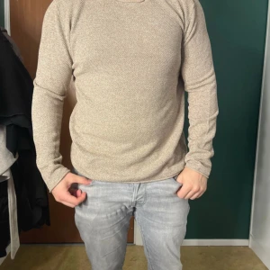 Beige stickad tröja från Selected Homme - Säljer en beige stickad tröja från Selected Homme. Tröjan har en enkel och clean design med rund halsringning och långa ärmar. Perfekt för lager-på-lager och passar till både jeans och chinos.