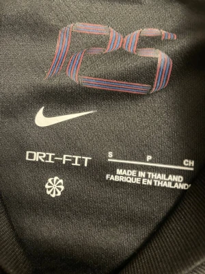 Svart FC Barcelona Nike fotbollströja S - FC Barcelona fotbollströja från Nike i svart med röda och blå sidopaneler. Tröjan har korta ärmar, klassisk krage och tryckta detaljer som klubbmärke, Nike-logga och Spotify sponsor. Materialet är lätt och ventilerande polyester, perfekt för match eller träning.
