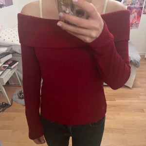 Mörkröd offshoulder ribbad tröja - Snygg mörkröd offshoulder tröja med ribbad struktur och långa ärmar. Tröjan har en bred kant upptill och passformen är slim och materialet känns mjukt och stretchigt. Är storlek S men passar också XS