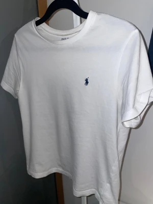 Vit t-shirt från Polo Ralph Lauren - Vit t-shirt från Polo Ralph Lauren  Tillverkad i mjuk bomull som känns skön mot huden. Storlek M i barnstorlek alltså 10-12 år. Har växt ur den så därför billigt pris. Det är bara att ställa frågor om du har någon!