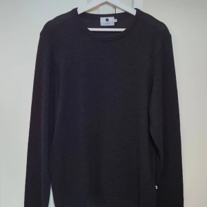 Marinblå stickad tröja från NN07 XL - Marinblå långärmad tröja från NN07 i modellen Collin, storlek XL. Tröjan har en rund hals och är tillverkad av en mix av polyakryl, bomull och linne. Den har en diskret ribbad struktur som ger en snygg och enkel look.