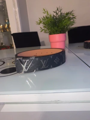 Svart  bälte med monogram - Säljer ett stilrent svart  bälte med klassiskt monogrammönster och en stor -spänne i silver. Bältet är gjort av skinn och har en rak, bred form som ger en lyxig vibe. Perfekt för dig som vill ha en ikonisk accessoar med tydlig stil.